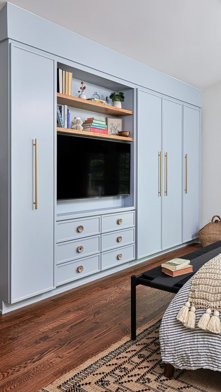 a powder blue wall cabinet with brass hardware and storage above the TV