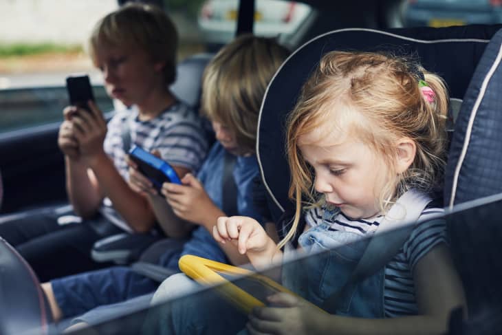 Three siblings using electronic tablets in the car