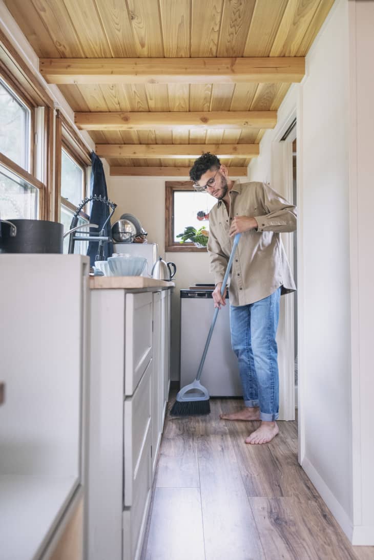 Young man sweeping floor in kitchen of tiny house