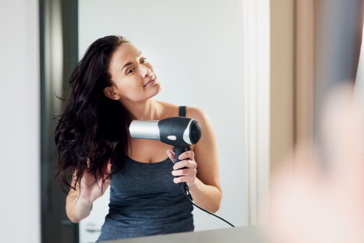 woman blowdrying her hair in front of a mirror in the bathroom