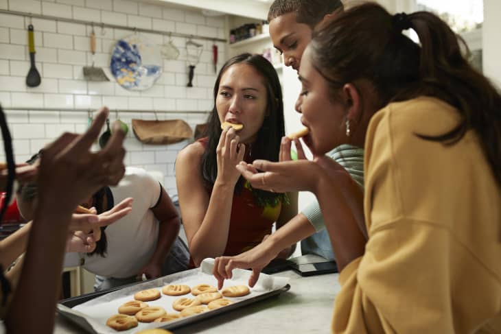 Young friends eating fresh baked cookies on kitchen island at home