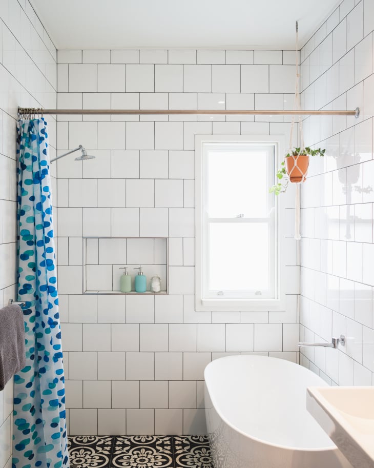 Wet room style bathroom with shower and bath. Black and white patterned floor, white tiled walls, blue and white shower curtain