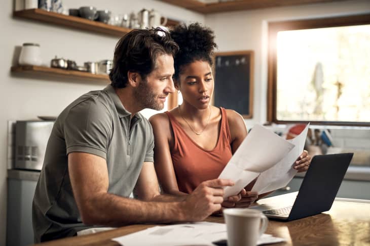 couple looking at paperwork and laptop in kitchen, light coming in through window, coffee mug on counter
