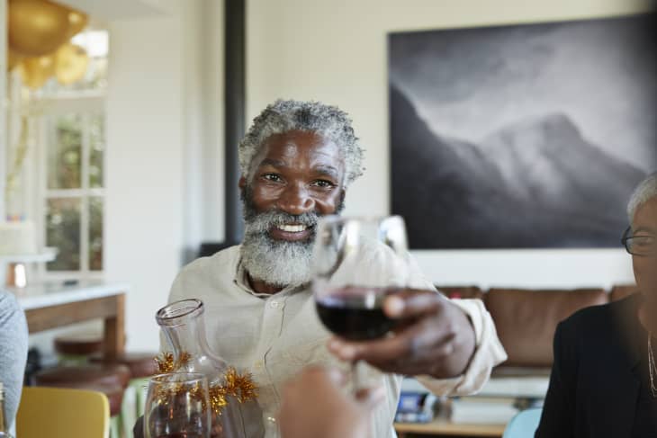 Portrait of smiling bearded man giving wineglass while sitting at home in Christmas party