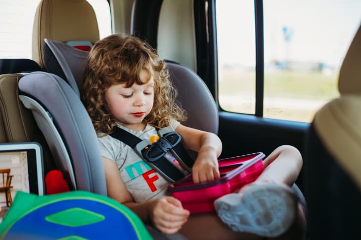 Young girl sitting in a car seat and eating lunch on a road trip