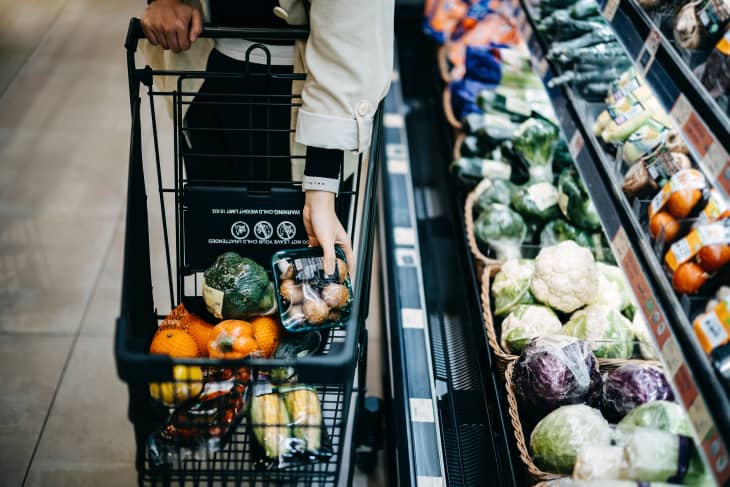 Close up of woman's hand shopping for fresh groceries in supermarket and putting a variety of organic vegetables in shopping cart