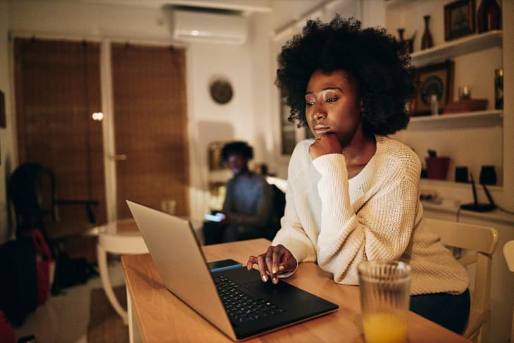 Beautiful African American woman studying in the living room on a laptop computer while living with her boyfriend.