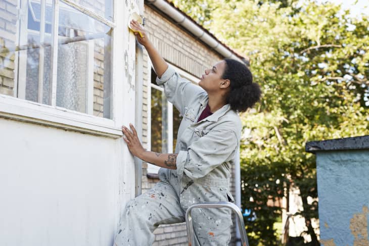 Woman repairing the outdoor window trim on her house