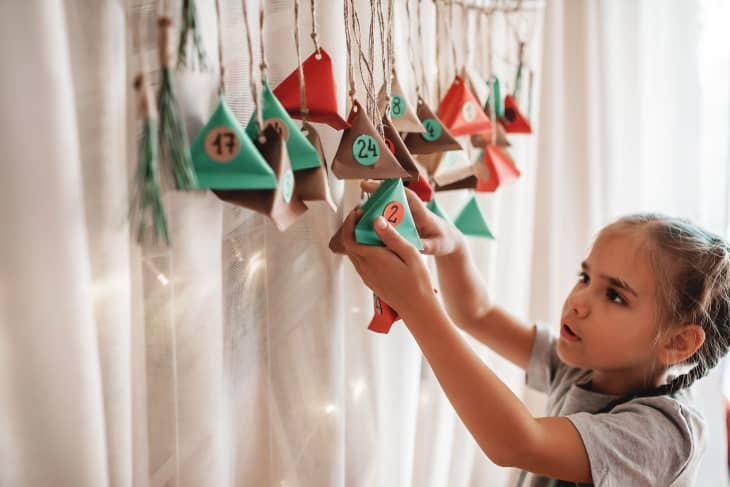 Cute little kid opening handmade advent calendar with color paper triangles.