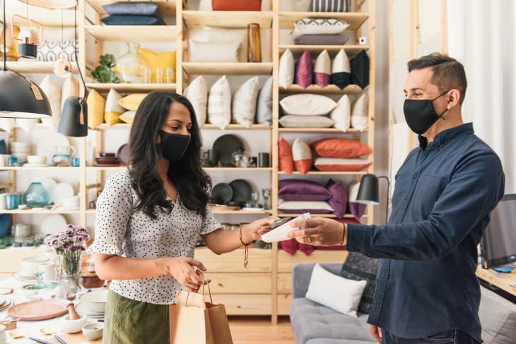 Masked shopper and store owner making purchase with credit card