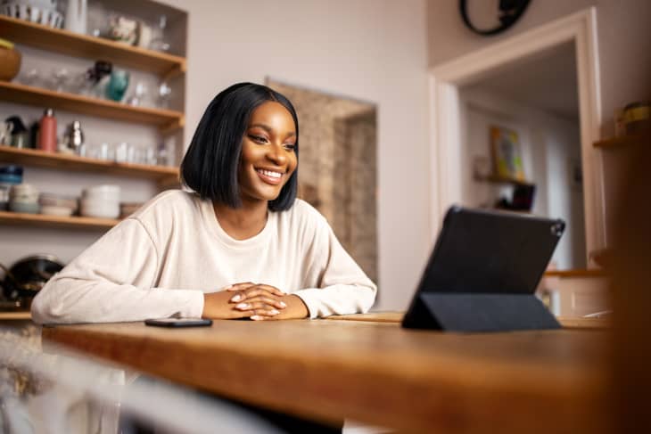 Beautiful young woman sitting at the table using digital tablet for making video call.