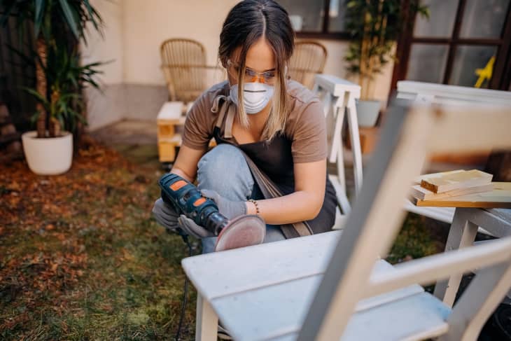 woman wearing protective mask sanding chair in back yard