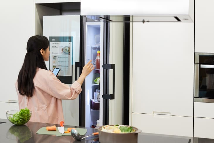 woman opening a smart fridge while holding her phone