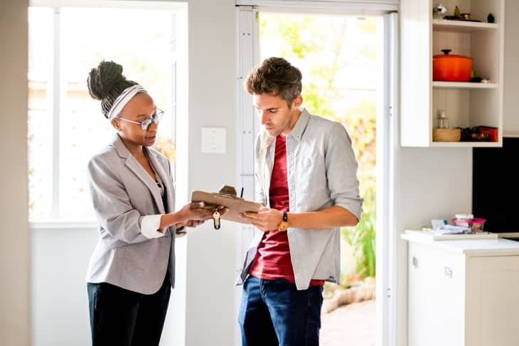 Young man signing new home contract with female real estate agent holding a clipboard