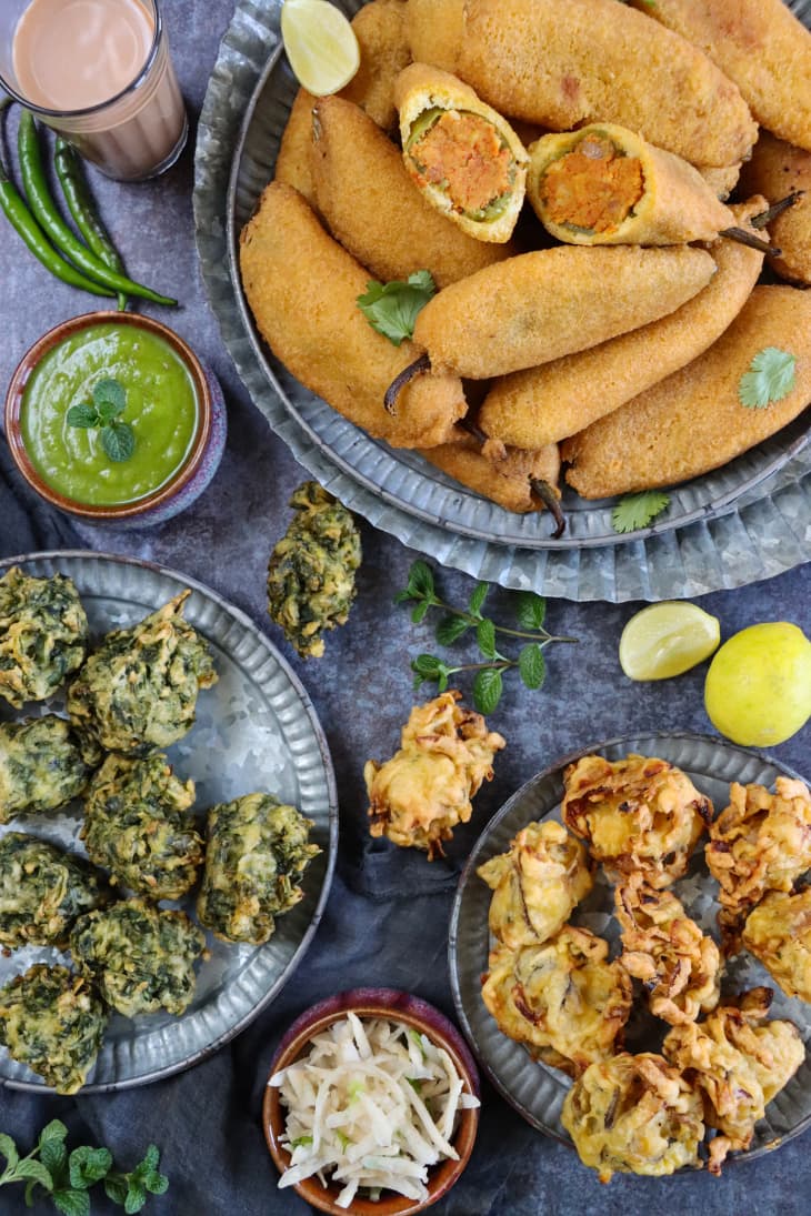 Stock photo showing a close-up, elevated view of a batch of homemade, fried mirch pakora (green chilli fritters) stuffed with an aloo mix, palak pakora (spinach fritters) and crispy, deep fried onion bahjees.