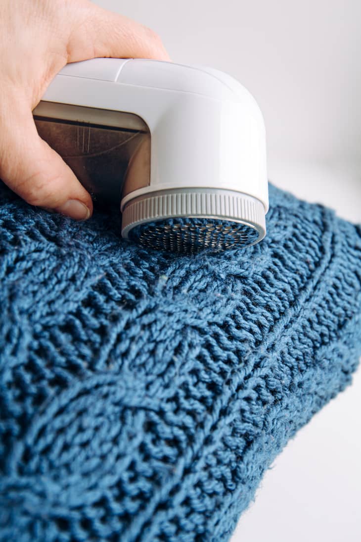 fabric shaver being used on blue cable knit sweater