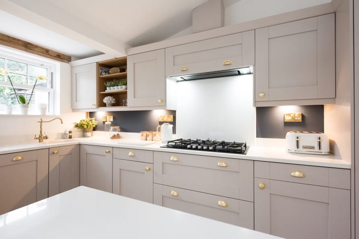 An interior view of a taupe, champagne coloured shaker style fitted kitchen diner with gold handles, quartz island, gas cooker hob, toaster