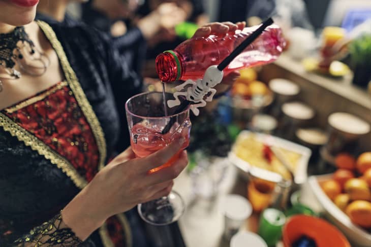 woman enjoying Halloween Party preparing colorful scary juice drink in a glass skull chalice.