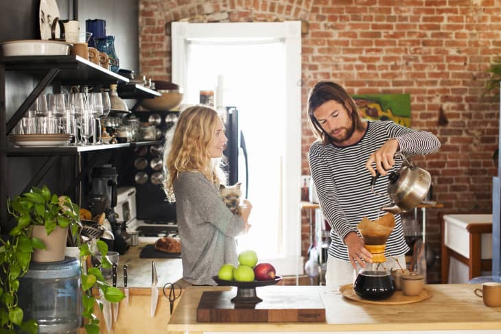 young couple making morning coffee in their kitchen while woman cradles small dog