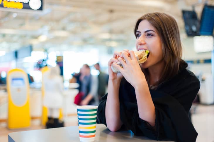 Young woman in airport, drinking coffee and eating a sandwich