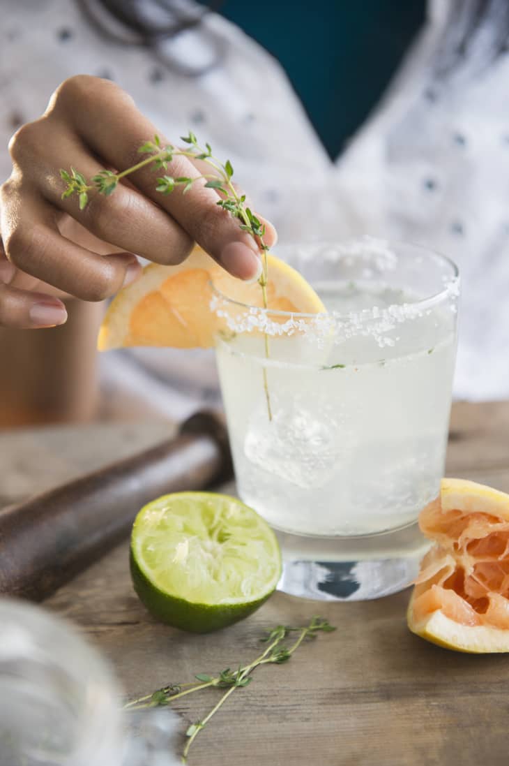 Woman adding a sprig of thyme to her citrus-based cocktail