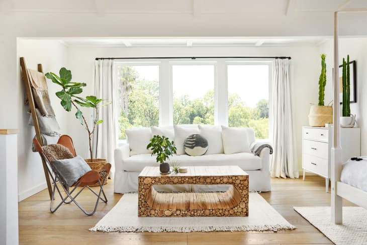 Four post bed and dresser in a beautiful white rustic modern design farmhouse tiny house bedroom with a white linen sofa and cactus on dresser.