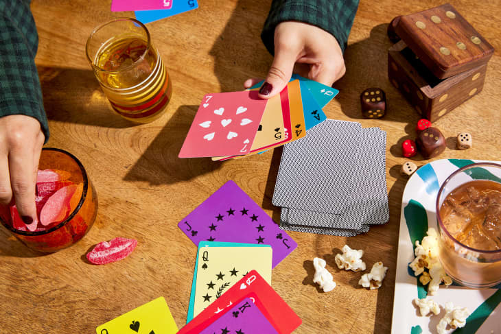 Hands of someone playing cards at table. The cards are bright and colorful. Snacks and other games on table