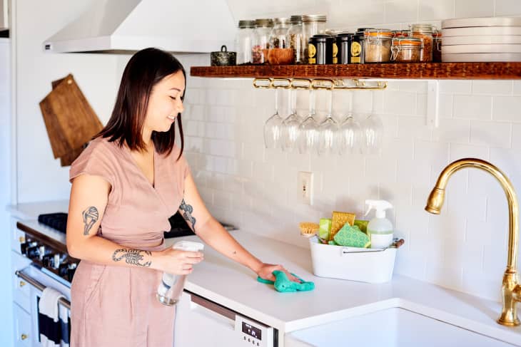 A person cleaning a kitchen counter with a cloth and spray bottle