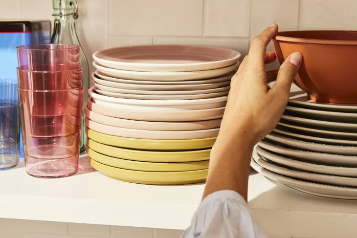 colorful stacks of plates, glasses, bowls on shelf. Someone is arranging, putting one away, or taking one out