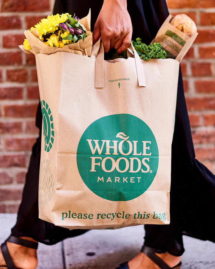 Woman holding Whole Foods bag filled with groceries while walking down the street