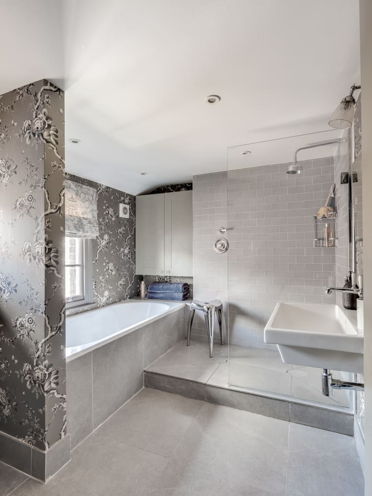 Elegant bathroom in shades of grey with floral wallpaper around bathtub area