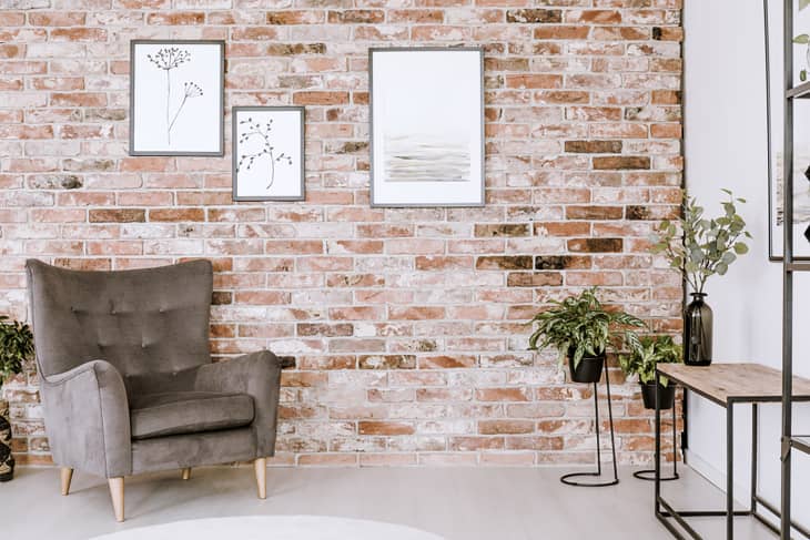 Living room interior with grey armchair, plants and posters on a red brick wall