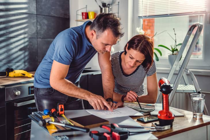 Couple standing by the table and looking at blueprints during kitchen renovation