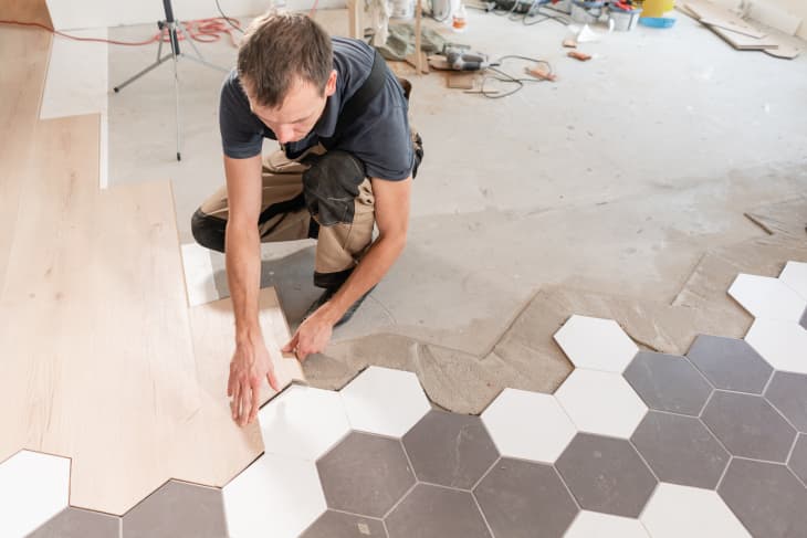 Male worker installing new wooden laminate flooring. The combination of wood panels of laminate and ceramic tiles in the form of honeycomb. Kitchen renovation