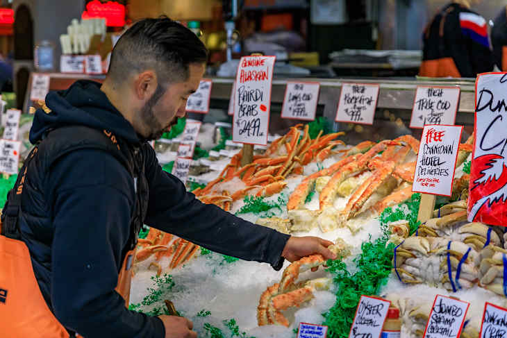 Seattle, United States - November 08, 2018: Fishmonger putting fresh crab legs on ice for sale at a stall at Pike Place Market with a customer in the background.