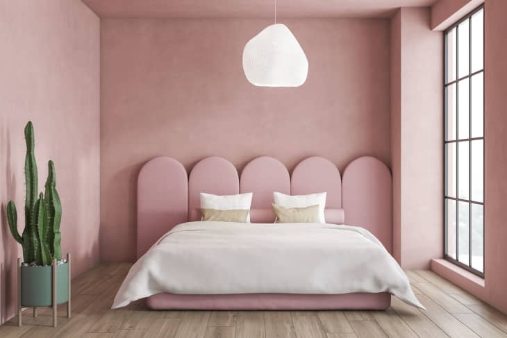 Interior of minimalistic bedroom with pink walls, wooden floor, master bed with original headboard and large window. 3d rendering