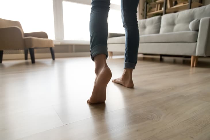 Close up of barefoot young woman in jeans feel comfortable walking on warm heated wooden floor at home, female step in her bare feet relaxing enjoy free sunny day in own modern apartment