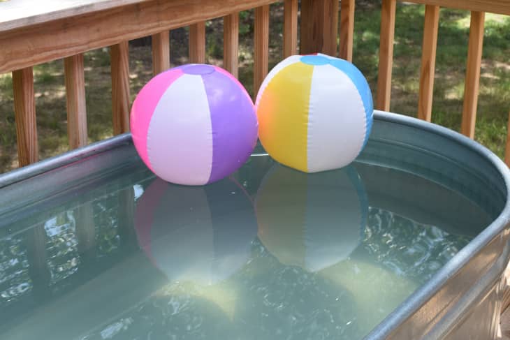 Two colorful beach balls float on the water in a stock tank swimming pool.