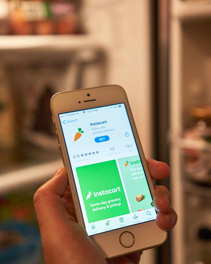 Portland, OR, USA - Mar 18, 2020: A woman checks the Instacart mobile app on her phone while opening the refrigerator. Instacart offers same-day grocery delivery and pickup service in the US &amp; Canada.