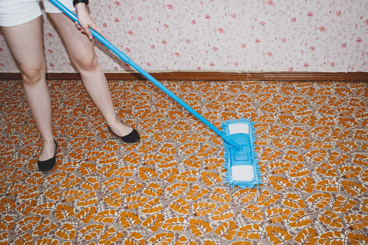 A woman cleans the floor with a MOP in a room covered with linoleum. The view from the top.