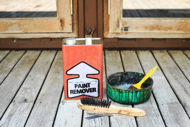 paint remover, a round bowl with paintbrush with black paint drips, and a scrubbing metal brush with a wood handle. Paint removal tools