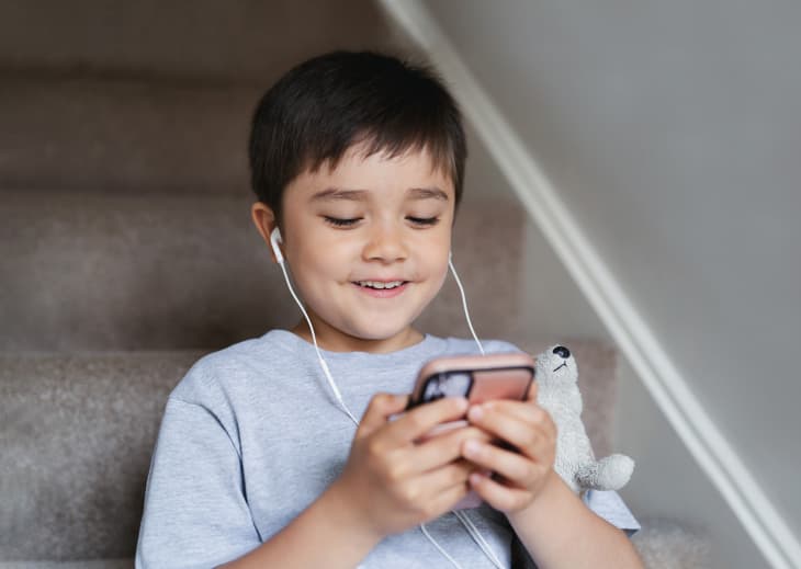 Candid shot child sitting on staircase wearing earphones listening relaxing music at home.Portrait happy boy playing games on mobile phone, Kid watching cartoon on cell phone.Children and Technology