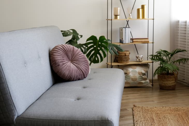 Minimalistic image, beige textile couch with round cushions and floor shelf over the blank wall background with a lot of copy space for text. Empty room interior with just a single sofa. Pintuck round pillow on sofa