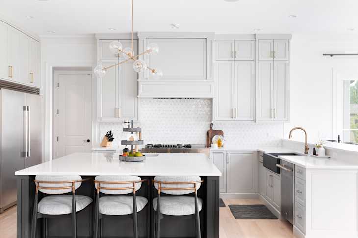 A luxurious kitchen with a large island, gold faucet and sputnik chandelier, stainless steel appliances, and white marble countertops.