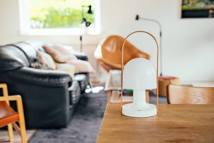 A white portable mushroom lamp with a handle on a table. Couch, chair, books, cosy room on the background