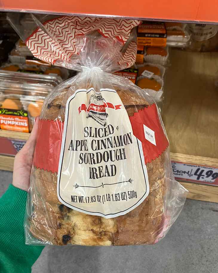 Sliced apple cinnamon sourdough bread in a clear bag, held in a hand, with other products in the background.