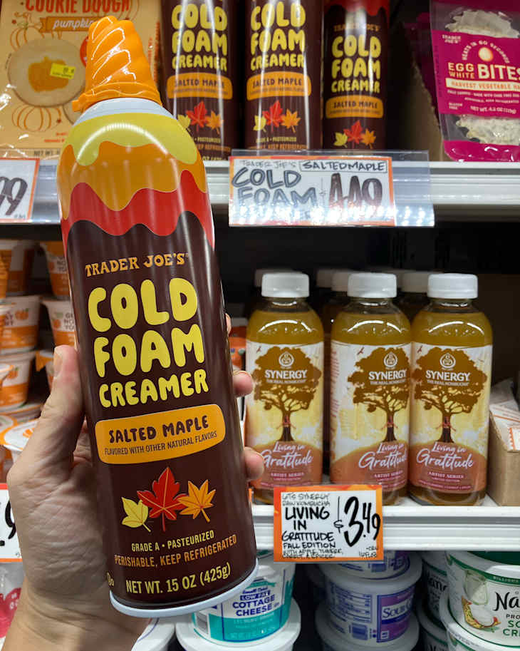 Trader Joe's Salted Maple Cold Foam Creamer in a hand, displayed on a shelf with various products and price tags.
