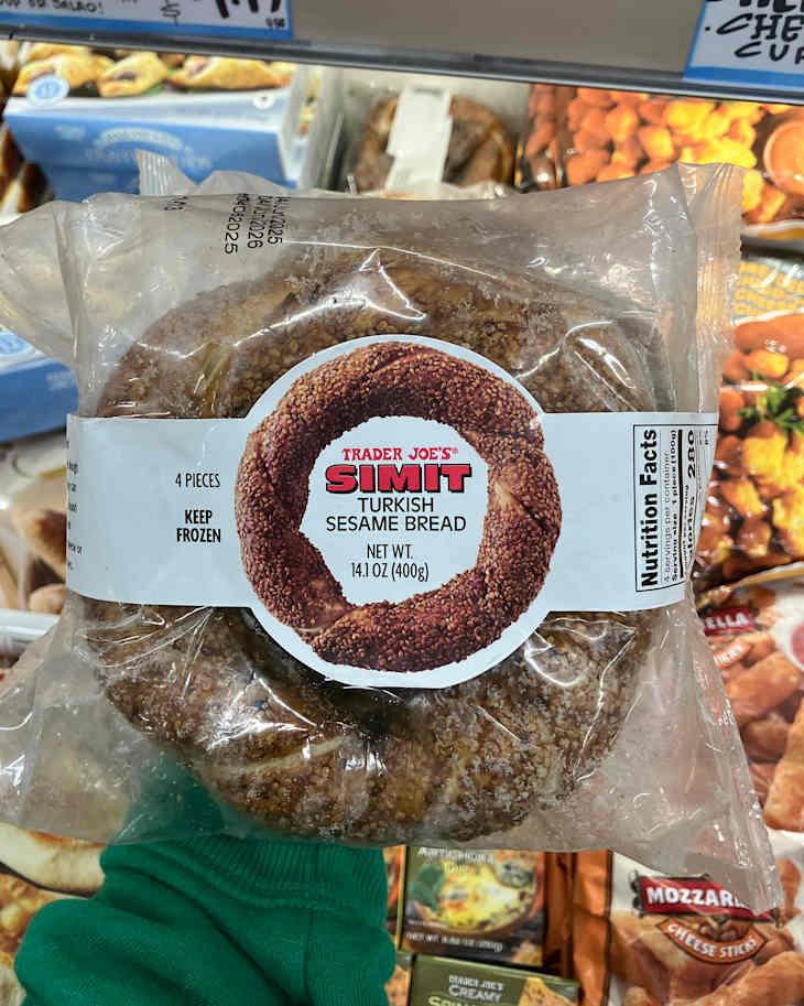 Frozen package of Trader Joe's Simit, Turkish sesame bread, with four pieces visible and a green sweater in the foreground.