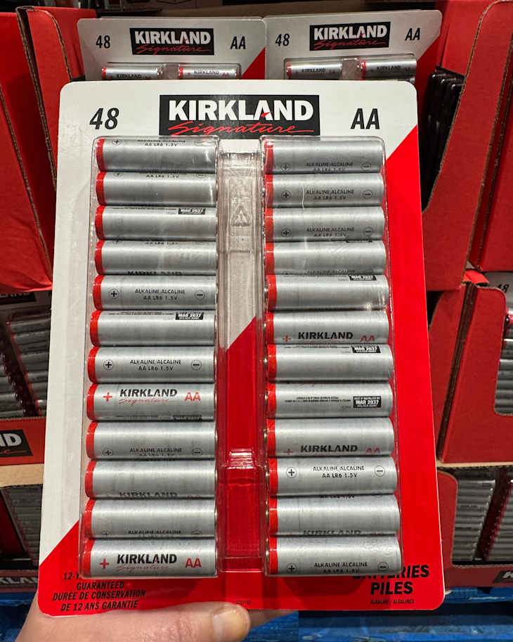 Pack of 48 Kirkland Signature AA alkaline batteries with red ends, displayed on a retail shelf.