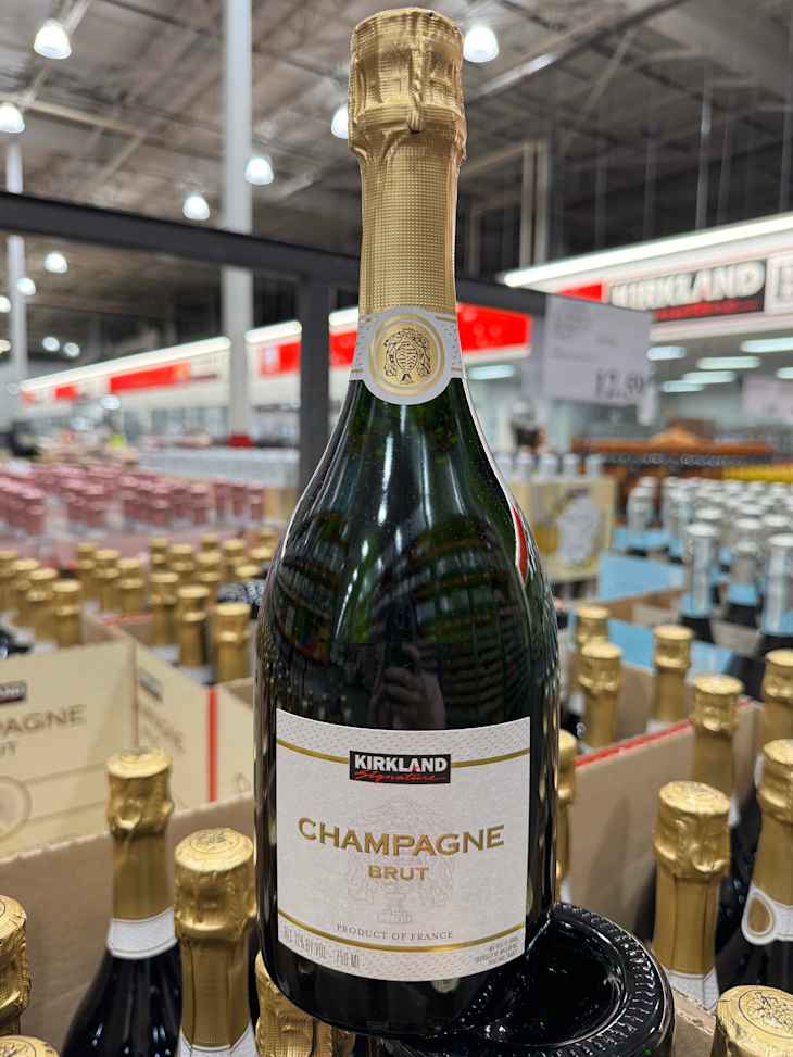 Bottle of Kirkland Champagne Brut with gold foil cap, displayed among other champagne bottles in a store.